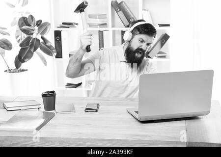 Homme barbu bureau écouteurs swing marteau sur ordinateur. Connexion internet lente. Logiciel obsolète. Décalage de l'ordinateur. Pour des raisons du retard de l'ordinateur. Comment fixer la traîne lente du système. La routine du bureau. Banque D'Images