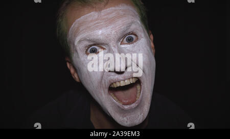 Clown Halloween man portrait. Close-up d'un fou, evil clowns font face. Maquillage visage blanc. Des cheveux verts. Rire effrayant. Modèle attrayant en costume d'Halloween. Fond sombre Banque D'Images