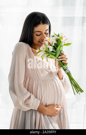 Smiling pregnant african american woman smelling bouquet dans l'appartement Banque D'Images