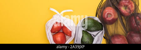Vue de dessus de pommes mûres, les tomates, l'avocat dans des sacs eco friendly isolé sur jaune, vue panoramique tourné Banque D'Images