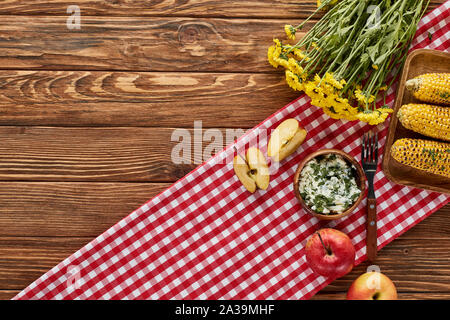 Vue de dessus du maïs grillé, pommes et fleurs jaune servi sur table en bois sur la serviette rouge Banque D'Images