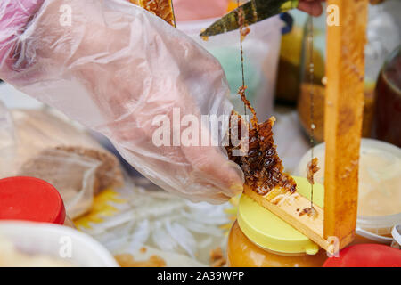 Prend la main un morceau de coupe de miel avec un couteau. La vente de miel faits maison sur le marché. Gros plan de la dégustation. Honey Farm. Banque D'Images