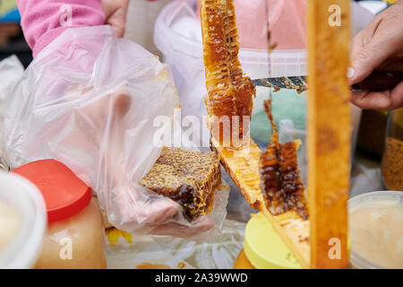 Prend la main un morceau de coupe de miel avec un couteau. La vente de miel faits maison sur le marché. Gros plan de la dégustation. Honey Farm. Banque D'Images