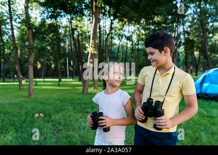 Happy boy looking at cute friend holding binoculars in park Banque D'Images