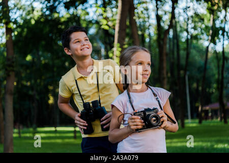 Enfants heureux jusqu'à la tout en maintenant les jumelles dans park Banque D'Images
