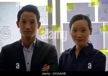 Portrait de l'équipe entreprises vietnamiennes confiant positif de deux debout devant un mur de verre recouvert de papier des rapports financiers Banque D'Images
