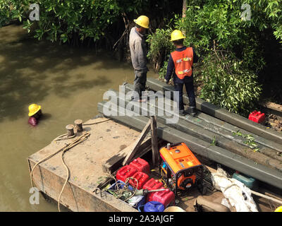 Équipe de travailleurs tirez des colonnes de béton hors de l'eau sur le fer au ponton. La reconstruction de la côte du fleuve, Thaïlande Banque D'Images