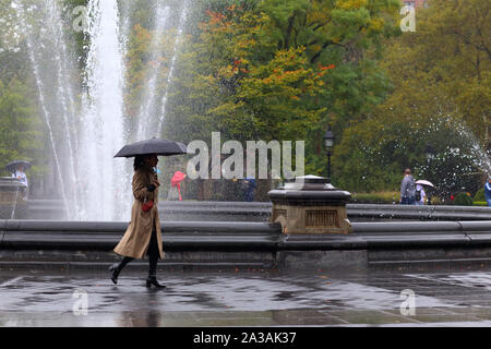 Une femme avec un parapluie promenades par le Washington Square Park fontaine sur un drizzy, rainy day à New York City Banque D'Images