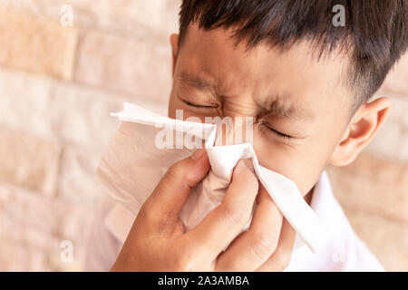 Aider un parent enfant à se moucher. Asian boy blowing le nez avec un mouchoir à la maison. Banque D'Images