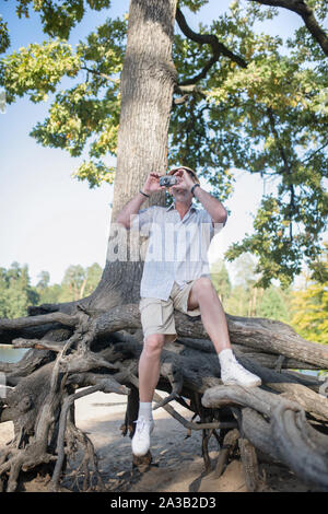 Homme portant courte séance sur les racines de l'arbre et la prise de photo Banque D'Images