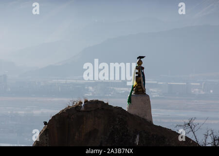 Un oiseau est perché au sommet d'un temple bouddhiste au monastère de Drepung, près de Lhassa, au Tibet. Dans l'arrière-plan sont les montagnes et la banlieue de Lhassa. Banque D'Images