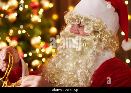 Le Père Noël ouvre un sac de cadeaux, assis près de l'arbre de Noël décoré avec des lumières - Joyeux Noël et bonnes fêtes ! Banque D'Images