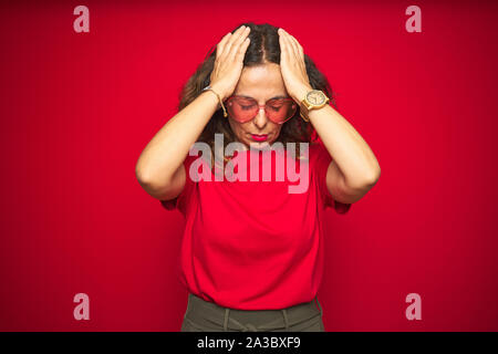 L'âge moyen senior woman wearing mignon lunettes en forme de coeur rouge sur fond isolés souffrant de maux désespérés et stressé car la douleur et Banque D'Images