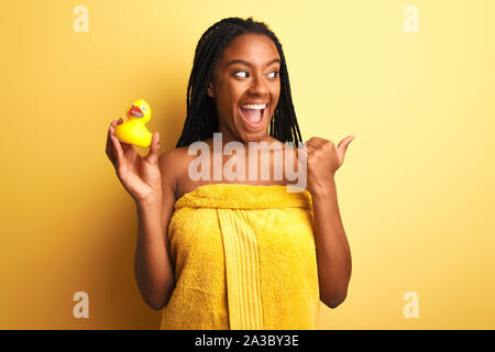 African woman holding serviette de douche canard sur fond jaune isolé et de pointage montrant avec le pouce jusqu'à la côte avec plaisir Banque D'Images