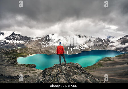 Man in red jacket est à la recherche dans le lac à Ala-Kul Tian Shan avec nuages brouillard blanc à Karakol parc national, le Kirghizistan Banque D'Images