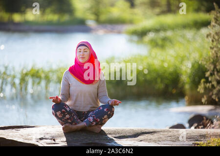 Jolie femme en hijab formation dans le parc, à méditer. Faire les exercices de yoga sur l'air frais et profiter de tôt le matin. Mode de vie sain Banque D'Images