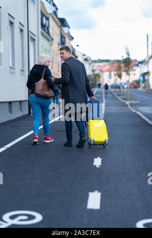 Couple en train de marcher dans la rue avec une valise comme le jeune homme se retourne comme si l'attente de quelqu'un dans un concept de voyage Banque D'Images