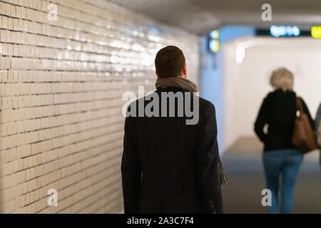 L'homme en manteau à la suite d'une femme à travers un tunnel couvert ou le métro dans un gros plan sur son dos Banque D'Images