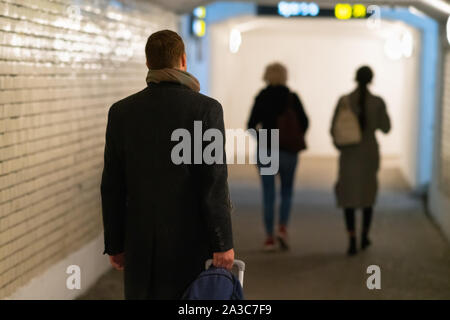 Homme marchant à travers un passage inférieur tirant une valise comme il suit deux femmes avant lui dans un concept de billet Banque D'Images