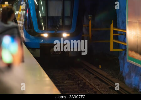 Inner city Blue train ou en métro entre dans une gare aux côtés d'une plate-forme avec les phares qui se reflète sur les murs Banque D'Images