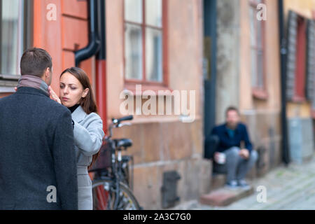 Jeune femme des vêtements de son mari de redressage sur la rue regardé en arrière-plan par un flou figure sur une porte Banque D'Images