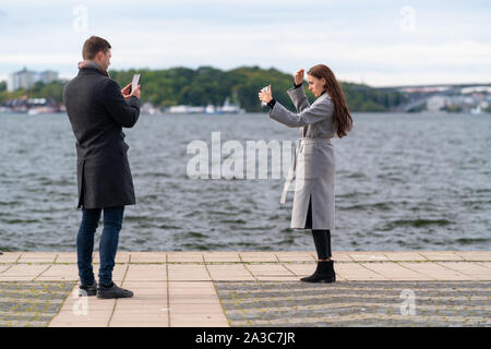 Jeune couple de prendre des photos sur un téléphone mobile comme la femme frappe un poser sur une promenade de bord de mer sur une froide journée d'hiver Banque D'Images