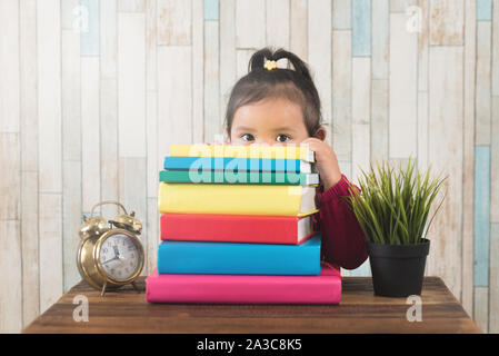 Cute little asian girl peeping de derrière la pile de livres. Concept de l'éducation, développement de l'enfant et couriousity Banque D'Images