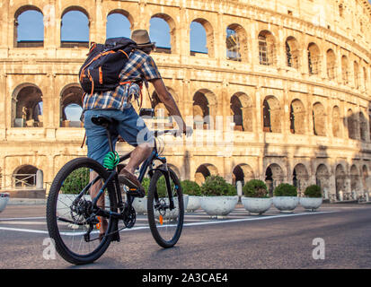 Heureux jeune homme avec le vélo touristique portant chemise et hat au Colisée à Rome, Italie au lever du soleil. Banque D'Images