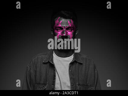 Découvrez ce qui est à l'intérieur de vous. Close up portrait of young man isolé sur fond de studio noir. Néon lumineux sur le visage. Thème Halloween effrayant, regarder, octobre vacances, concept d'horreur. Banque D'Images