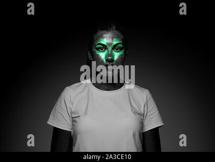 Découvrez ce qui est à l'intérieur de vous. Close up portrait of young woman isolé sur fond de studio noir. Néon lumineux sur le visage. Thème Halloween effrayant, regarder, octobre vacances, concept d'horreur. Banque D'Images