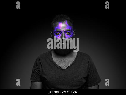 Découvrez ce qui est à l'intérieur de vous. Close up portrait of young man isolé sur fond de studio noir. Néon lumineux sur le visage. Thème Halloween effrayant, regarder, octobre vacances, concept d'horreur. Banque D'Images