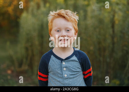 Closeup portrait of young red-haired mignon beau garçon d'âge préscolaire. Adorable enfant debout à l'extérieur de l'automne journée d'automne. Happy smiling kid à l'extérieur. Un Banque D'Images