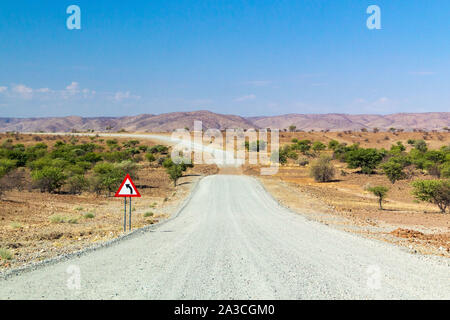 Route de gravier sinueuses avec panneau de circulation qui mène à travers le magnifique paysage du Kaokoland, la Namibie, l'Afrique Banque D'Images