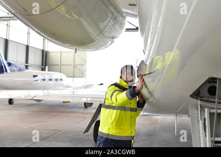 Mécanicien d'aéronefs inspecte et vérifie la technologie d'un jet dans un hangar à l'aéroport Banque D'Images