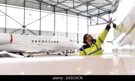 Mécanicien d'aéronefs inspecte et vérifie la technologie d'un jet dans un hangar à l'aéroport Banque D'Images