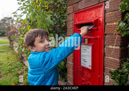 Un jeune garçon posts une lettre dans une boîte aux lettres intégrée dans un mur. Banque D'Images