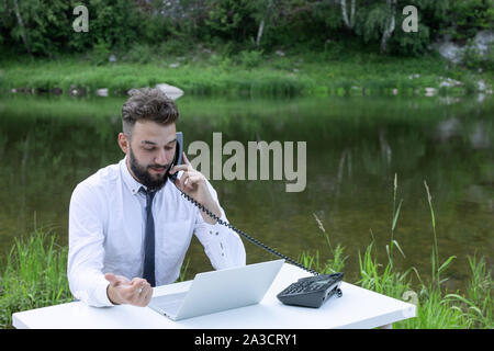 Offres de concept, travailler à l'extérieur du bureau, le travail à distance. barbu travaille derrière un coffre à l'air libre. demande par téléphone Banque D'Images