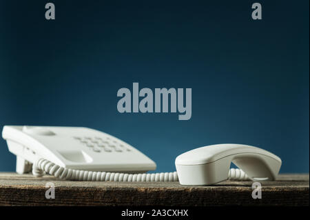 Low angle view of white téléphone fixe avec combiné décroché sur le bureau en bois rustique. Sur fond bleu marine. Banque D'Images