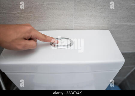 Close up of finger en poussant un bouton pour le nettoyage des toilettes à chasse d'eau des toilettes. Banque D'Images