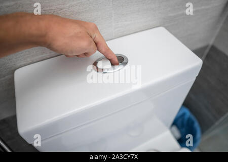 Close up of finger en poussant un bouton pour le nettoyage des toilettes à chasse d'eau des toilettes. Banque D'Images