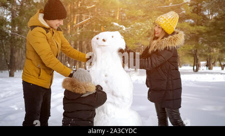 Balades d'hiver et de jouer avec l'enfant en fin de semaine. Famille heureuse mère, père et fils sont un bonhomme ensemble dans winter park. Banque D'Images