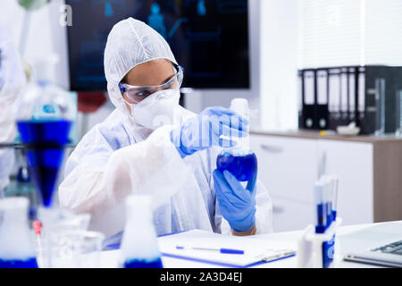 Les analyses des chercheurs d'un tube avec un liquide bleu à partir de laquelle la fumée sort. Entouré par d'autres tubes Banque D'Images
