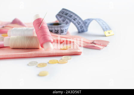 Accessoires de couture et tissu rose sur fond blanc. Tissu, fils de couture, l'aiguille, fermeture éclair, les boutons et la couture centimètre. Banque D'Images