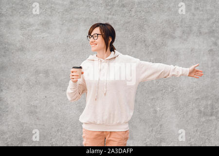 Jolie jeune femme en blanc, culotte et verres avec la tasse de café en papier pour aller dans ses mains, heureux et souriant. Immersive. Banque D'Images