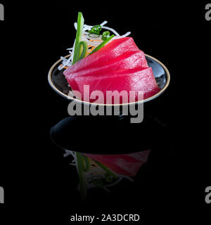 Sashimi de thon dans une plaque noire. Sur un fond noir avec la réflexion. Banque D'Images