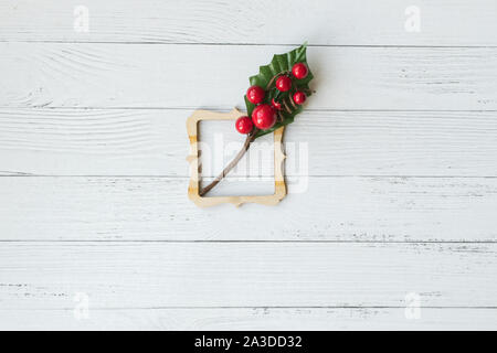 Noël arrière-plan de composition décorative avec cadre en bois et des branches avec des baies rouges sur planche de bois blanc. Bonne année. Carte. Copier l'espace. Banque D'Images