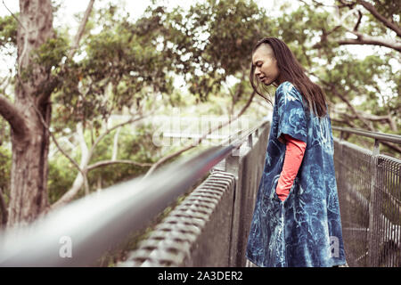 Mixed Race woman androgyne avec robe bleue regarde sur tree topwalk Banque D'Images