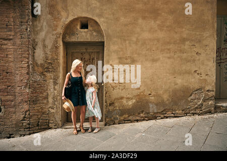 Jeune femme aux cheveux blonds hugging girl à chapeau de paille en se tenant sur le rue pavée de la vieille ville de Toscane Italie Banque D'Images