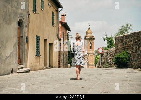 Vue arrière de la femme romantique se promener le long de l'ancienne rue avec maisons à simple chapelle confortable en Toscane Italie Banque D'Images