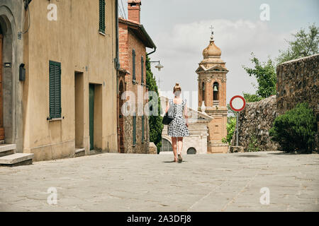 Vue arrière de la promenade femme marchant dans la rue pavée avec des maisons simples et l'interdiction de signer la circulation automobile avant de chapelle confortable en Toscane Italie Banque D'Images